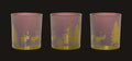 Three pink and gold candle holders with deer and tree design on a white background